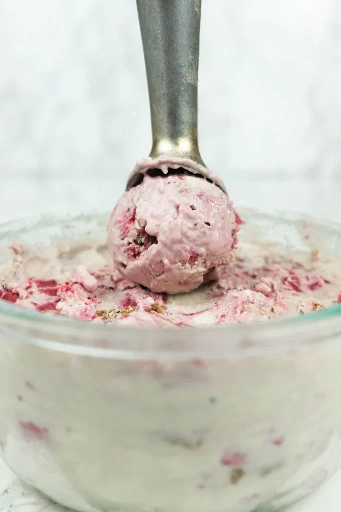 A metal ice cream scoop lifts a perfectly rounded scoop of no-churn vegan strawberry ice cream with granola chunks.
