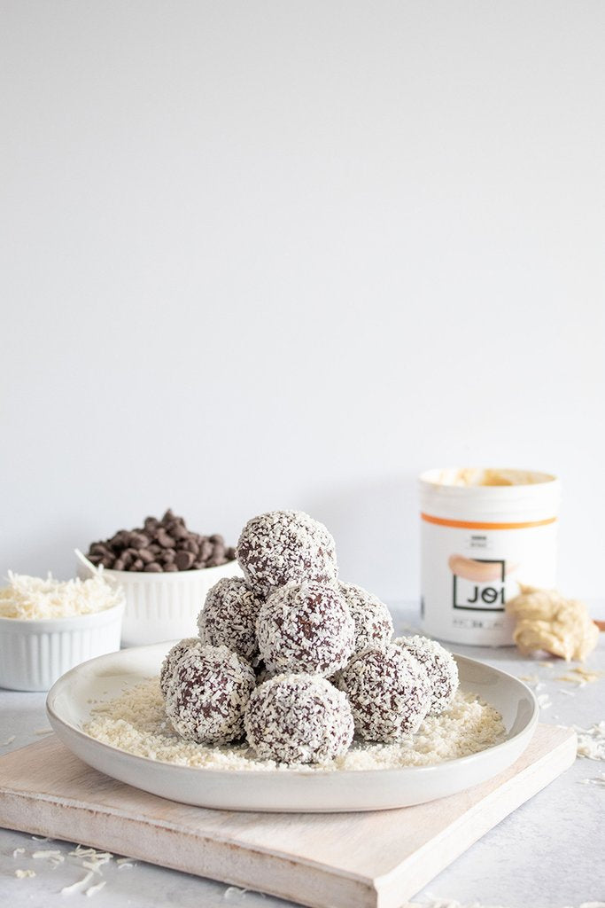 A plate of vegan chocolate coconut truffles made with JOI sits on a white table with chocolate chips and a JOI jar.