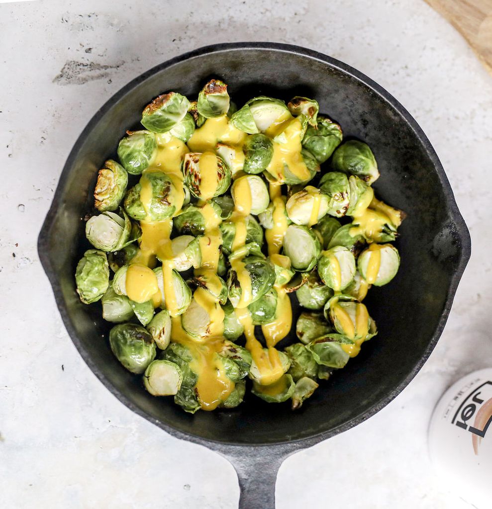 Dairy-free Brussels sprouts in a cast iron pan, drizzled with JOI creamy honey mustard sauce.