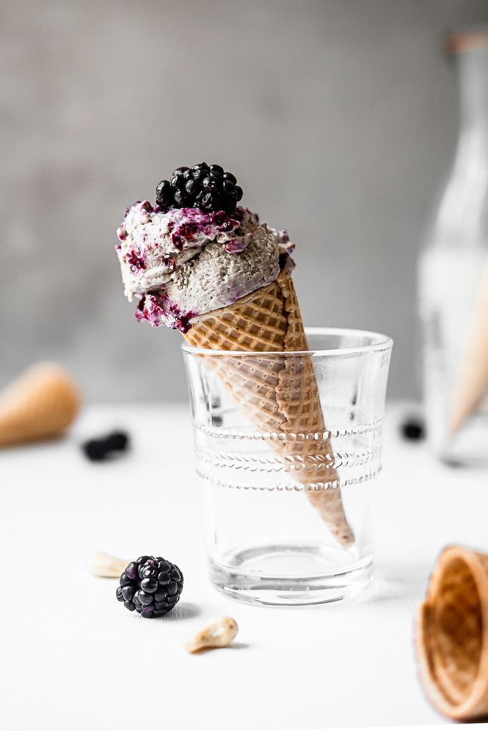 A waffle cone with JOI vegan blackberry nice cream, topped with fresh blackberries, rests in a glass.