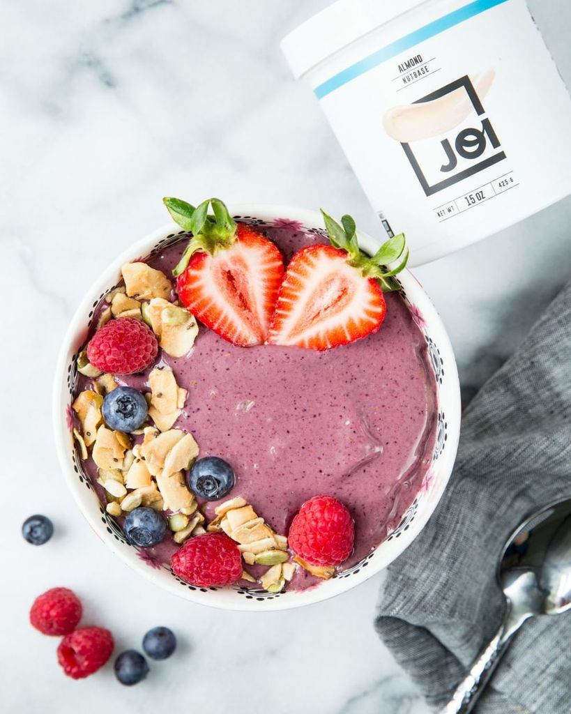 A vibrant berrylicious smoothie bowl made with JOI almond nutbase, topped with fresh fruit, granola, and seeds.