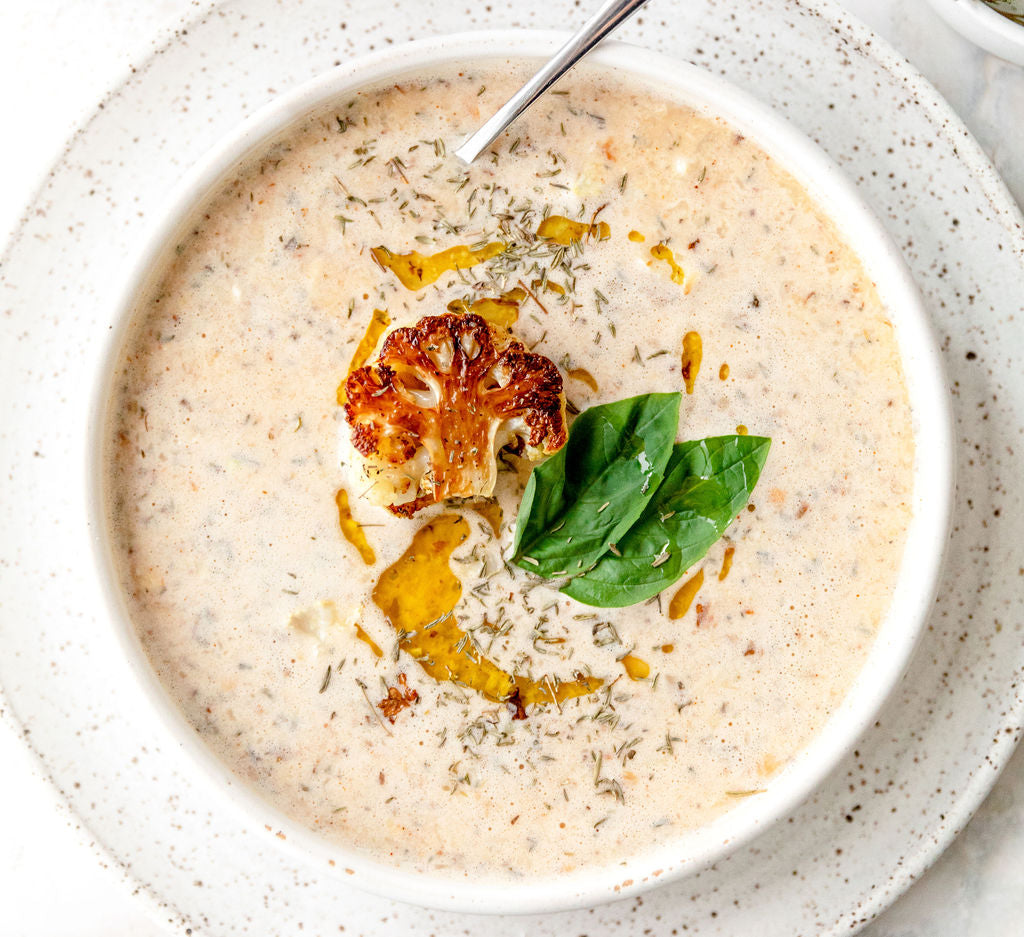 A bowl of creamy cauliflower soup, made with JOI plant bases, garnished with roasted cauliflower, herbs, and basil.