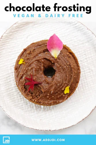 A delectable donut with rich vegan chocolate frosting made with JOI, garnished with flower petals, on a white plate.