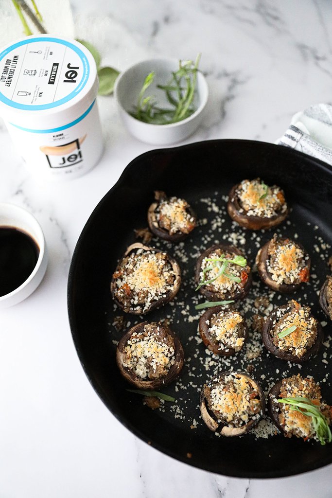 A white can of JOI plant base sits next to a black cast iron pan filled with tomato and tarragon stuffed mushrooms.