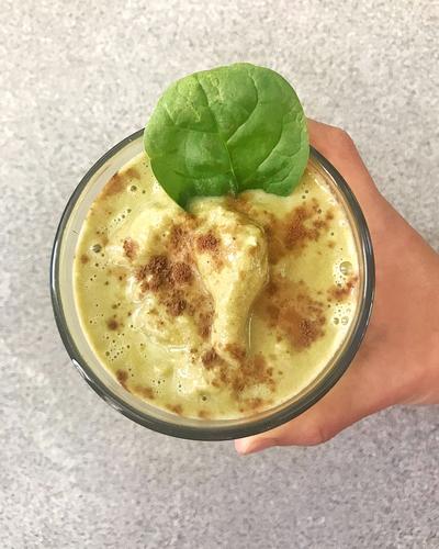 A hand holds a glass of a Caffeinated Spicy Mocha Smoothie, made with JOI plant base, topped with cinnamon and a spinach leaf.