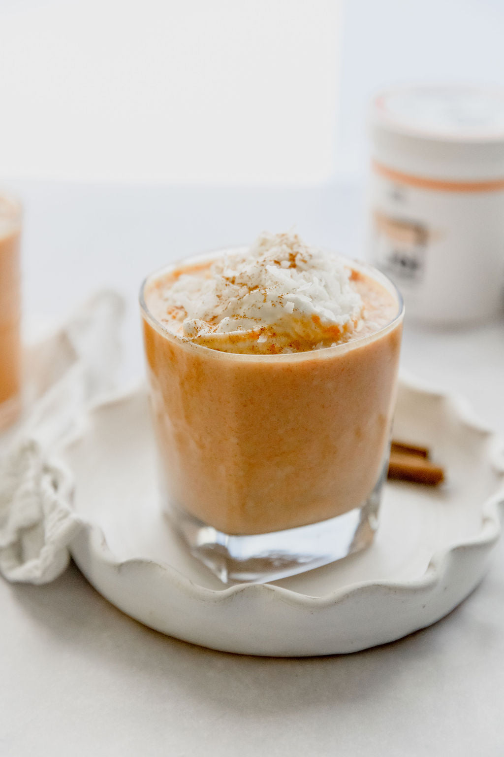 A carrot cake smoothie made with JOI plant base, topped with whipped cream and cinnamon, served on a white plate.