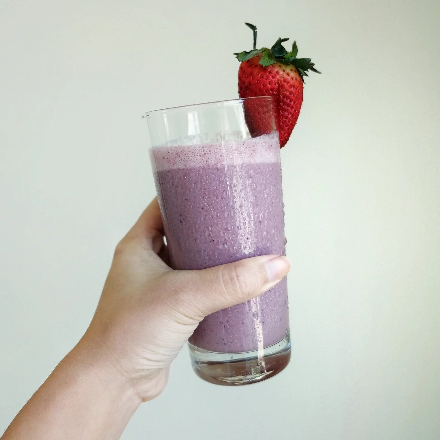A hand holds a tall glass of purple JOI plant-based smoothie, garnished with a fresh strawberry.