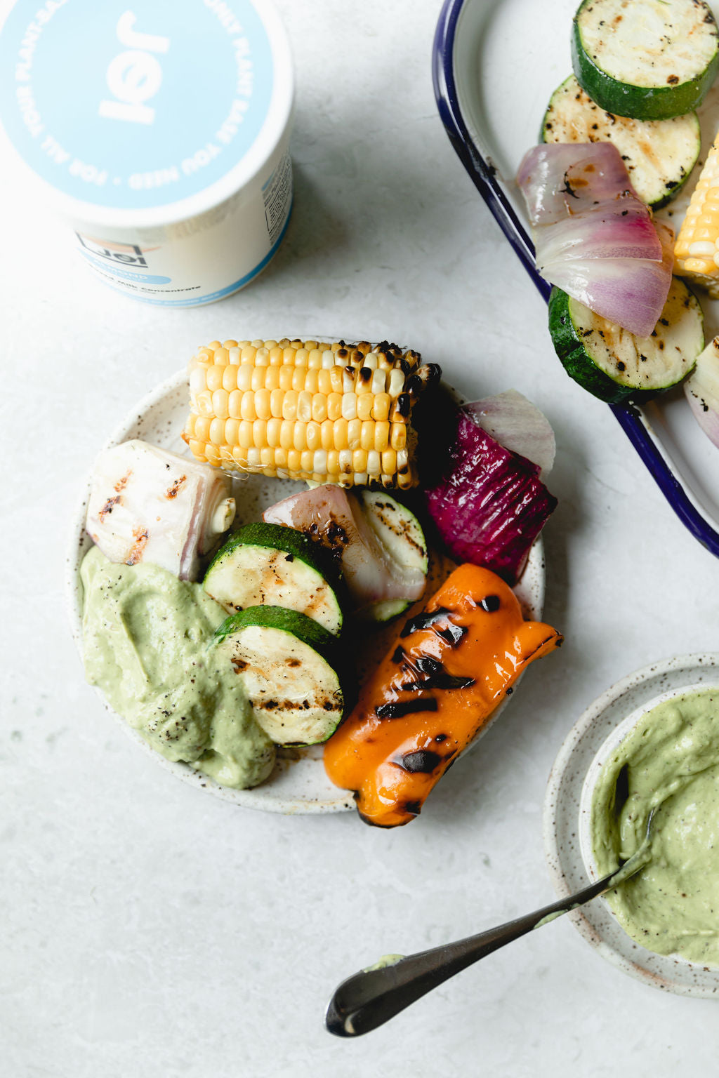 Grilled summer vegetables with creamy avocado dip and JOI plant base in a container.