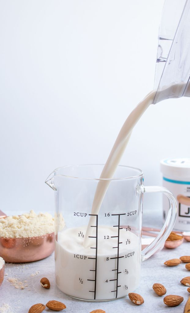 Vegan buttermilk made from JOI plant base is poured from a blender into a clear measuring cup, surrounded by almonds.