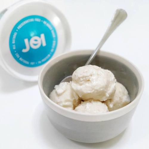 A grey bowl of creamy, white vegan vanilla ice cream made with JOI, with a spoon and the JOI container nearby.