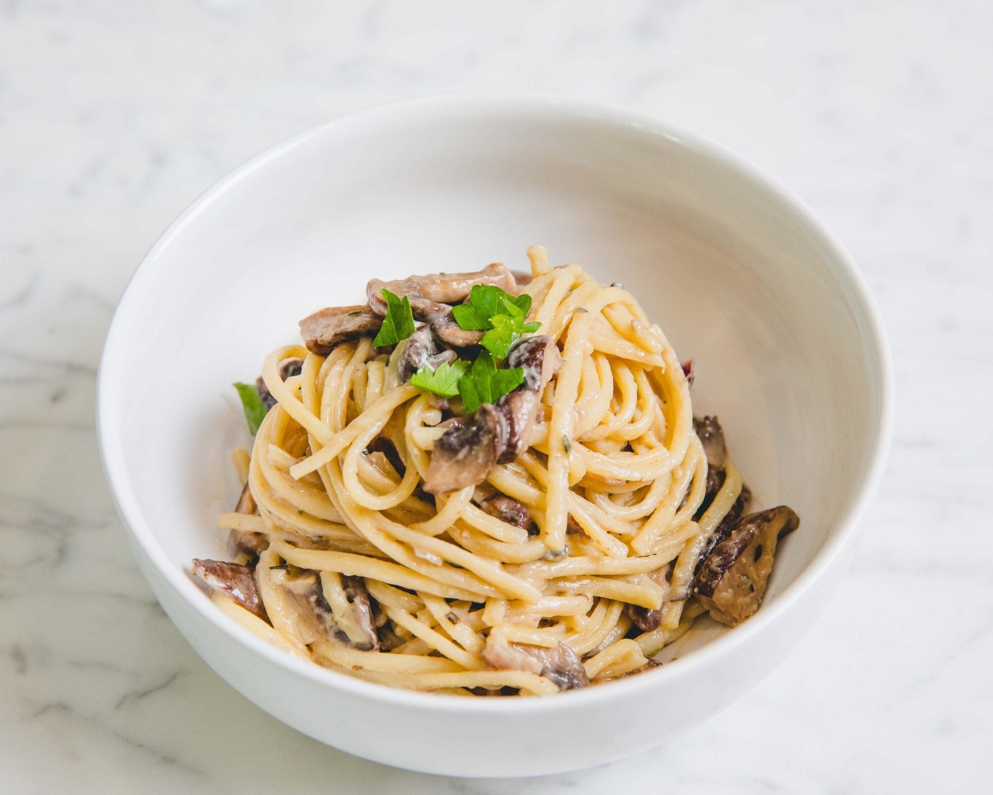A white bowl filled with creamy vegan mushroom pasta sauce made with JOI plant base, topped with fresh parsley.