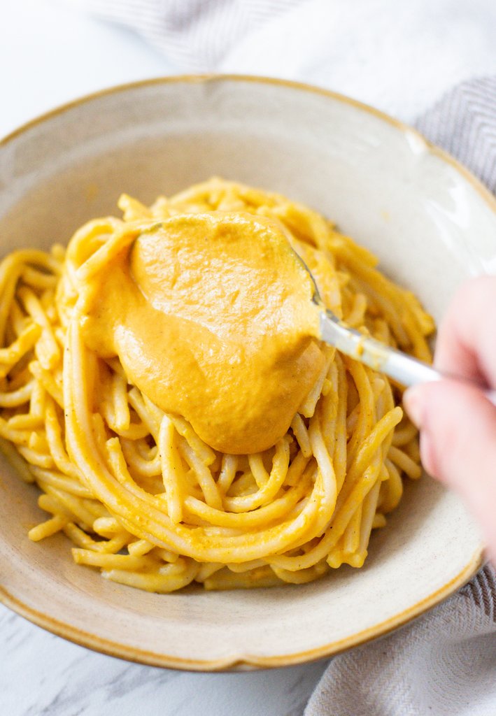 A creamy, orange vegan pumpkin alfredo sauce made with JOI is spooned over a bowl of pasta.