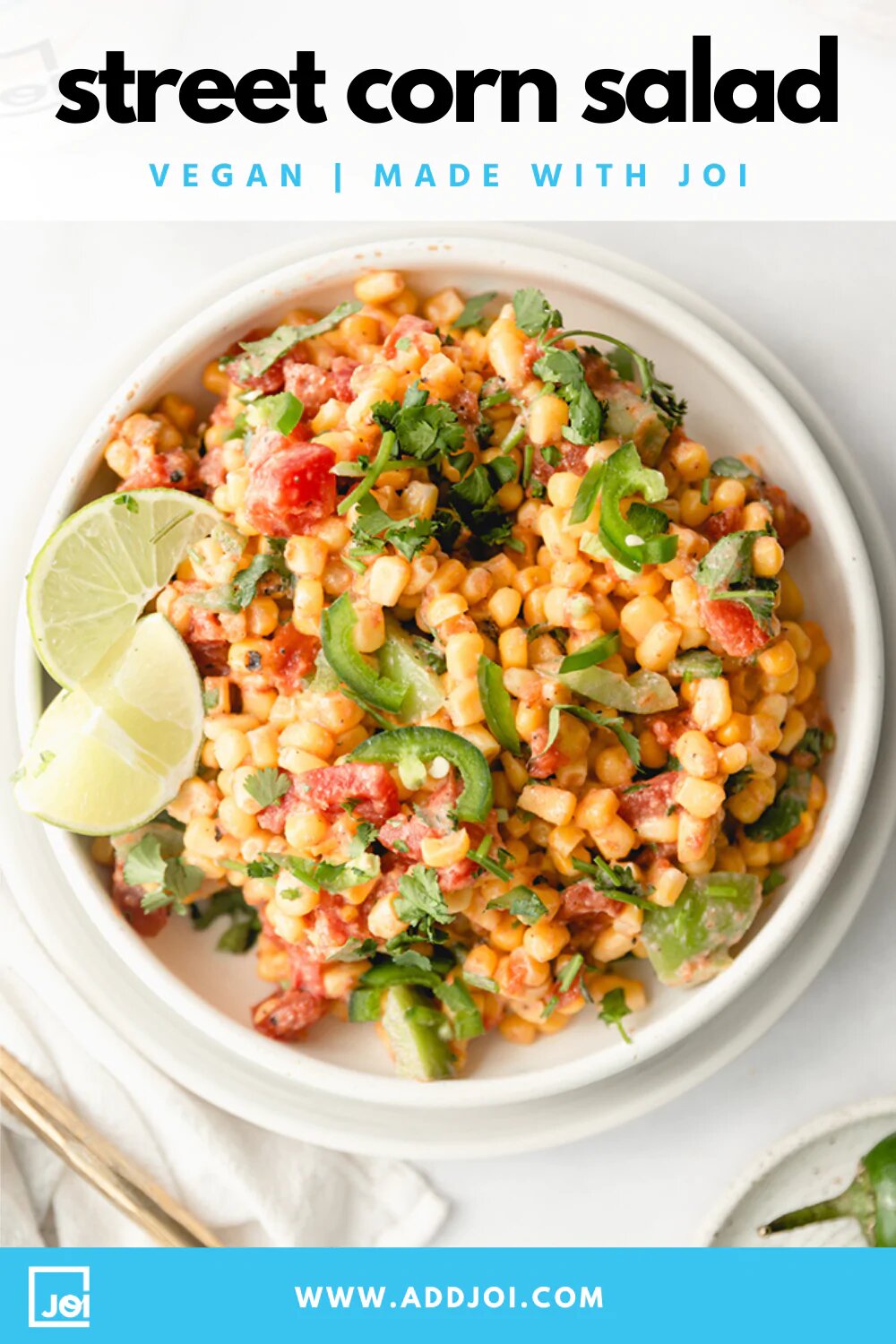 A white bowl of Street Corn Salad with creamy salsa made with JOI plant base, garnished with cilantro, jalapeños, and lime wedges.