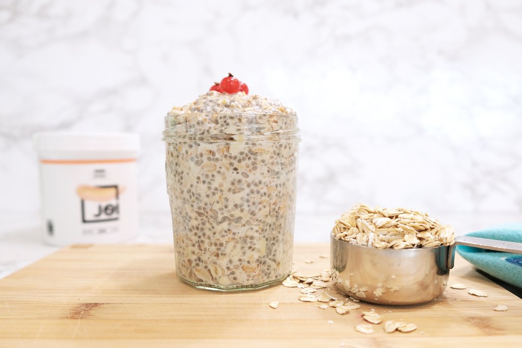Overnight oats in a glass jar topped with red berries, a JOI plant base container, and a measuring cup of rolled oats.