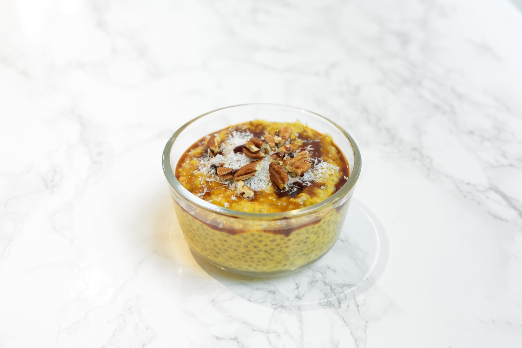 A glass bowl of creamy orange pumpkin chia pudding made with JOI plant milk concentrate, topped with pecans and coconut flakes.