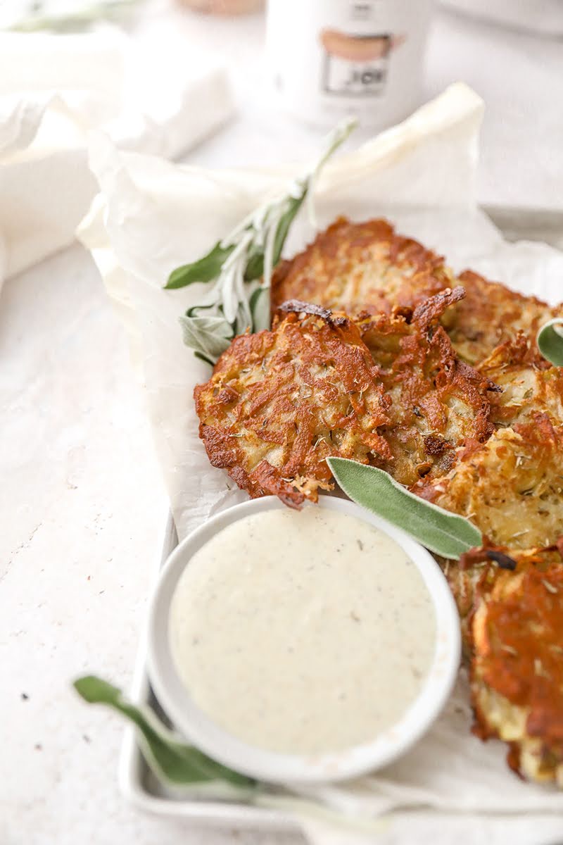 Crispy, dairy-free potato pancakes with fresh sage and a creamy JOI plant-based dip on a white platter.