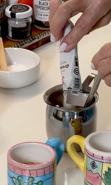A person adds JOI plant-based coffee creamer from a packet into a metal cup with a spoon.