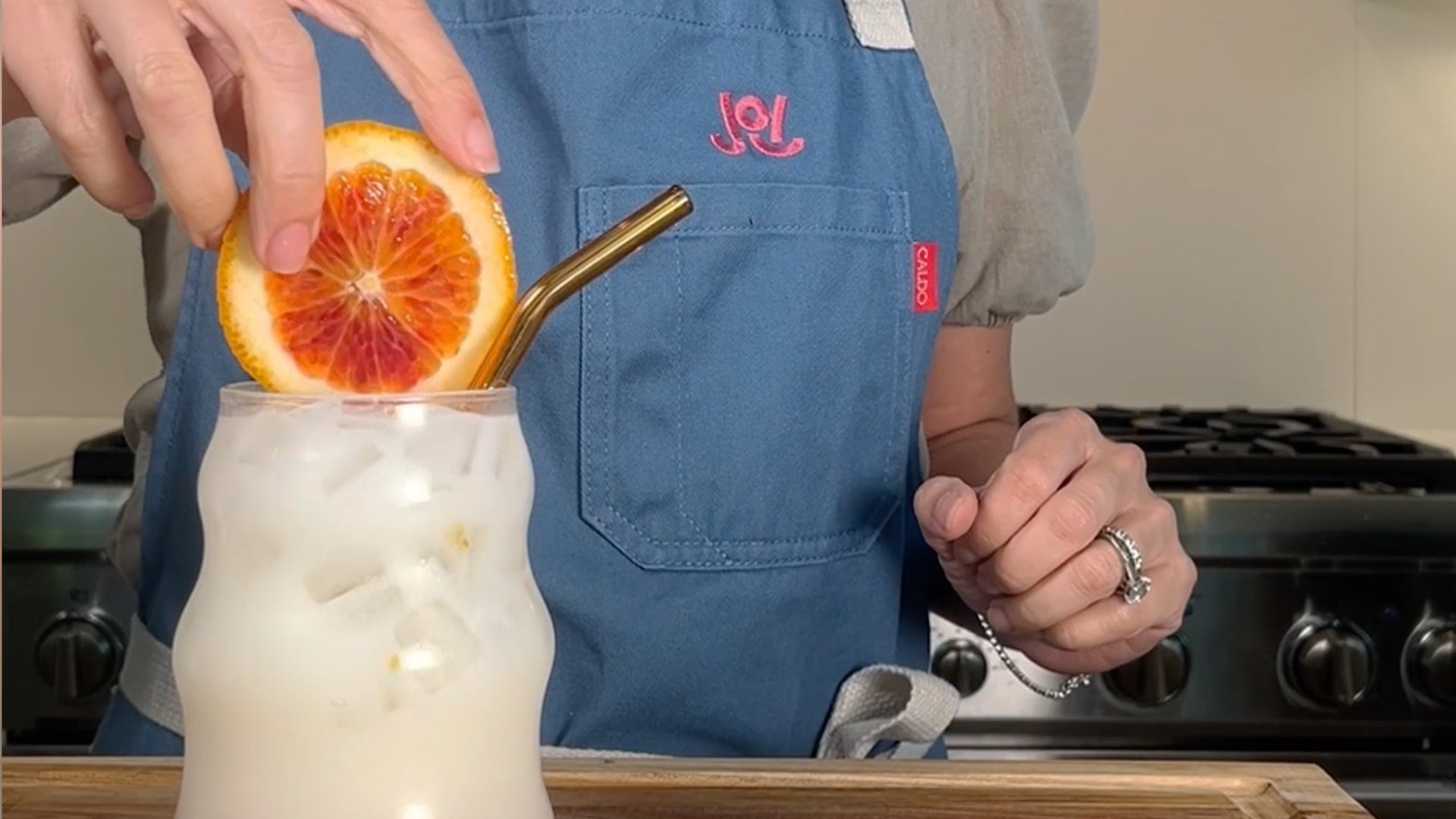 A hand garnishes a glass of JOI oat milk dirty soda with a blood orange slice and a metal straw.