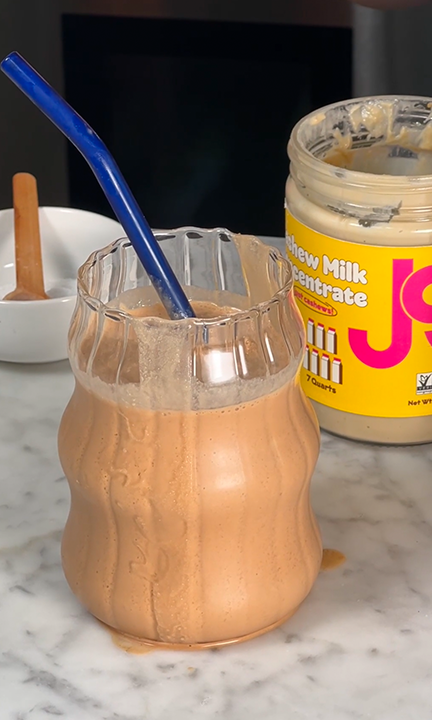 A JOI Blended Iced Protein Coffee, made with JOI Cashew Milk Concentrate, in a wavy glass with a blue straw.