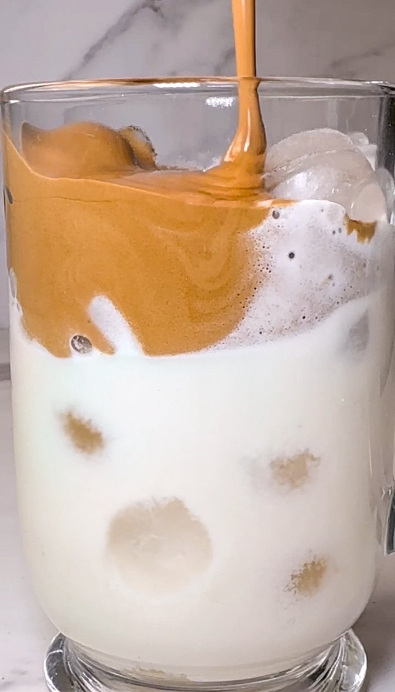 Thick, creamy whipped coffee made with JOI plant milk is poured over ice, creating a delicious dairy-free iced coffee.