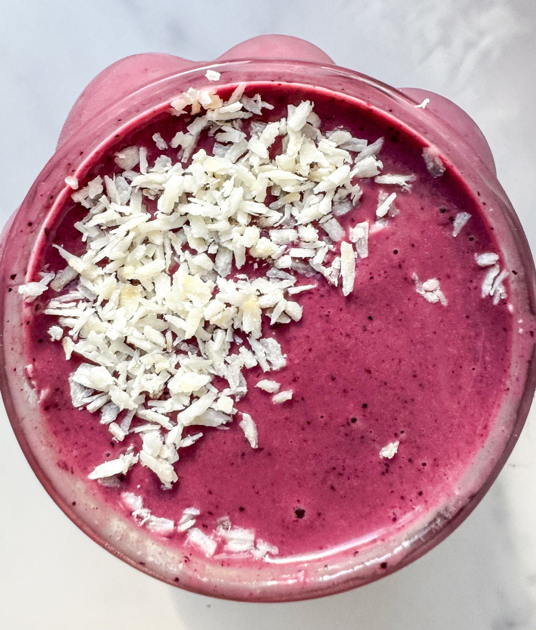 An overhead shot of a vibrant beet berry smoothie with JOI plant base, topped with white shredded coconut flakes.