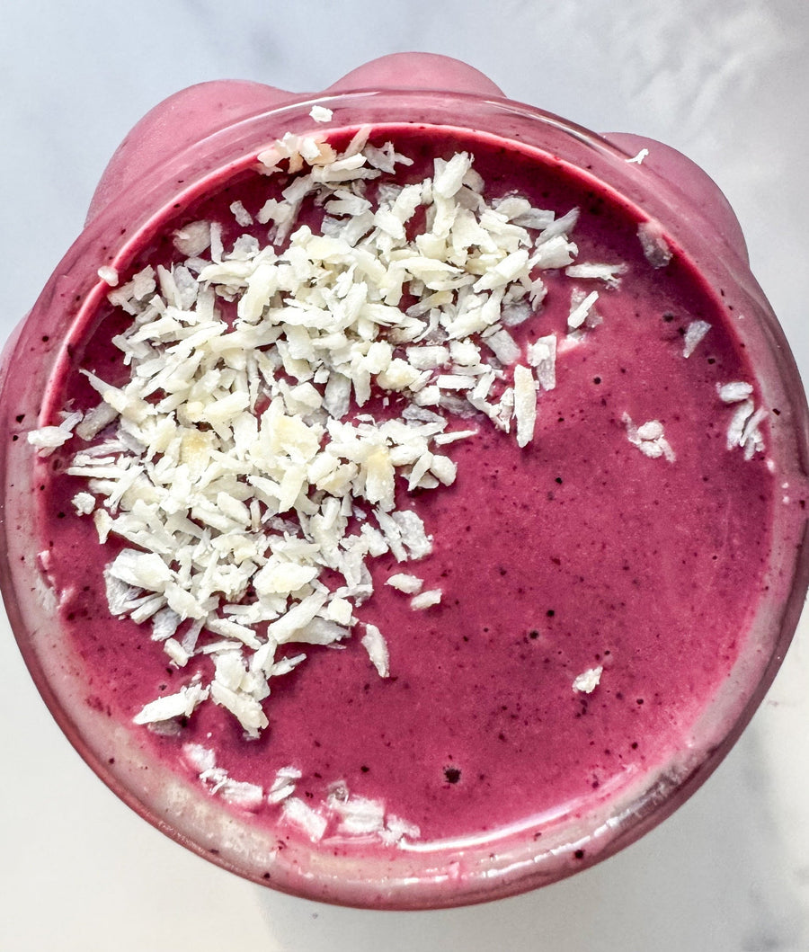 An overhead shot of a vibrant beet berry smoothie with JOI plant base, topped with white shredded coconut flakes.