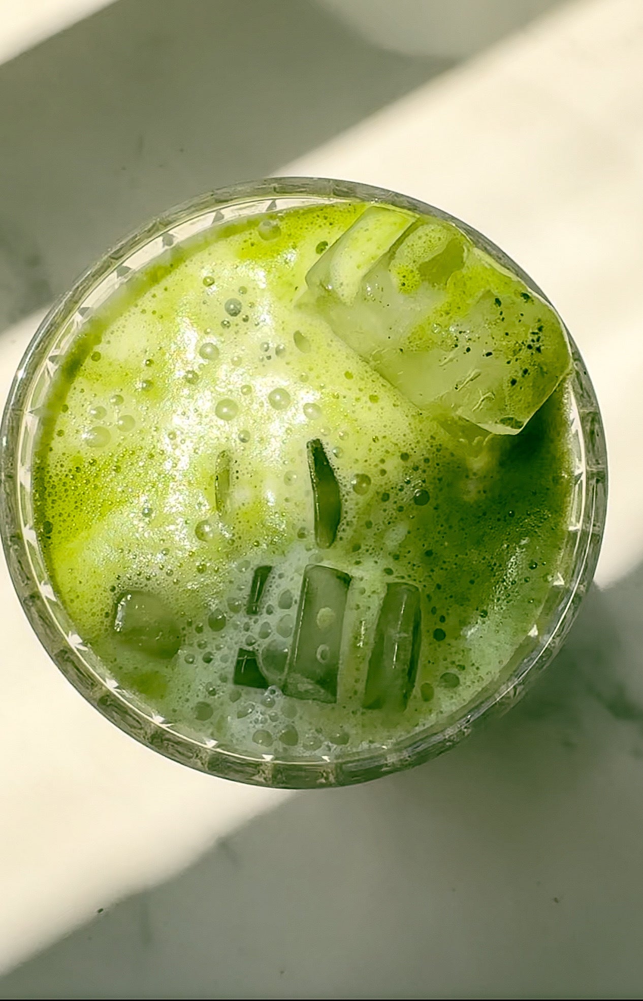 An overhead view of a vibrant green iced matcha latte, featuring JOI concentrate, with a foamy top.