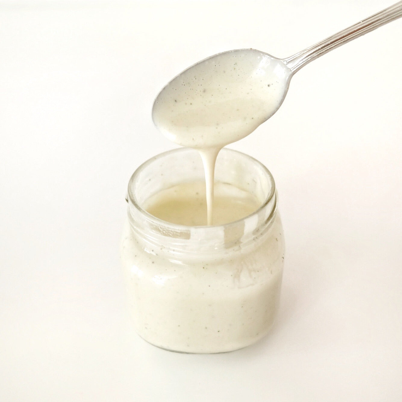 A spoon dripping creamy, off-white JOI dairy-free sour cream into a small glass jar.