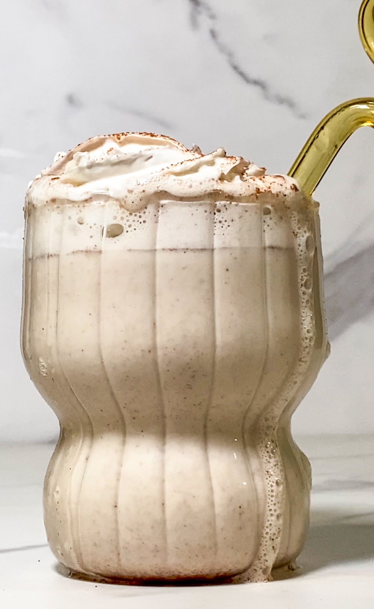 A festive JOI vegan holiday nog, topped with whipped cream and cinnamon, spills over the side of a glass.