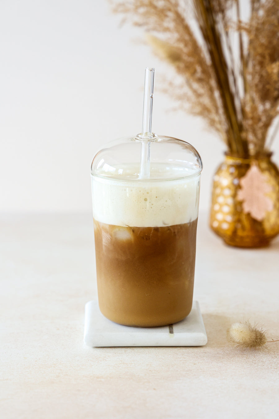 A tall glass of an iced vanilla oat milk latte made with JOI plant base, topped with foam.