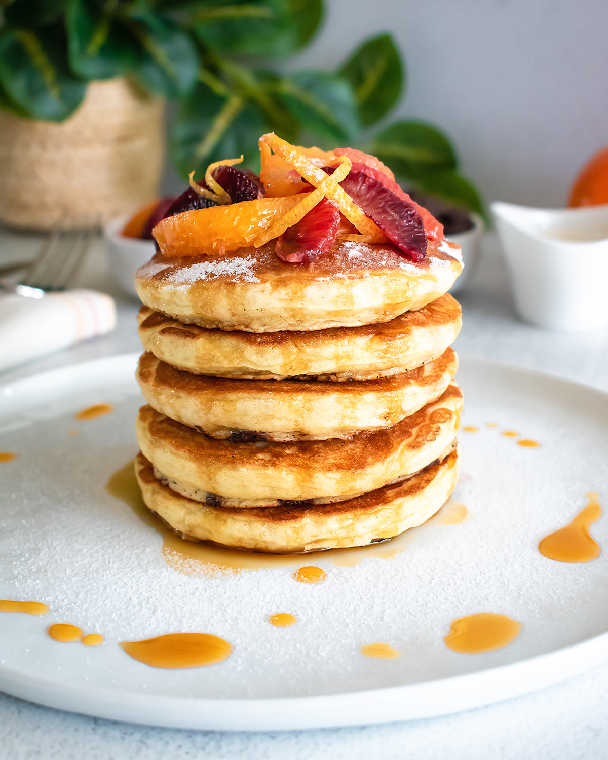 A stack of fluffy JOI vegan buttermilk pancakes with chocolate chips, topped with orange compote, powdered sugar, and syrup.