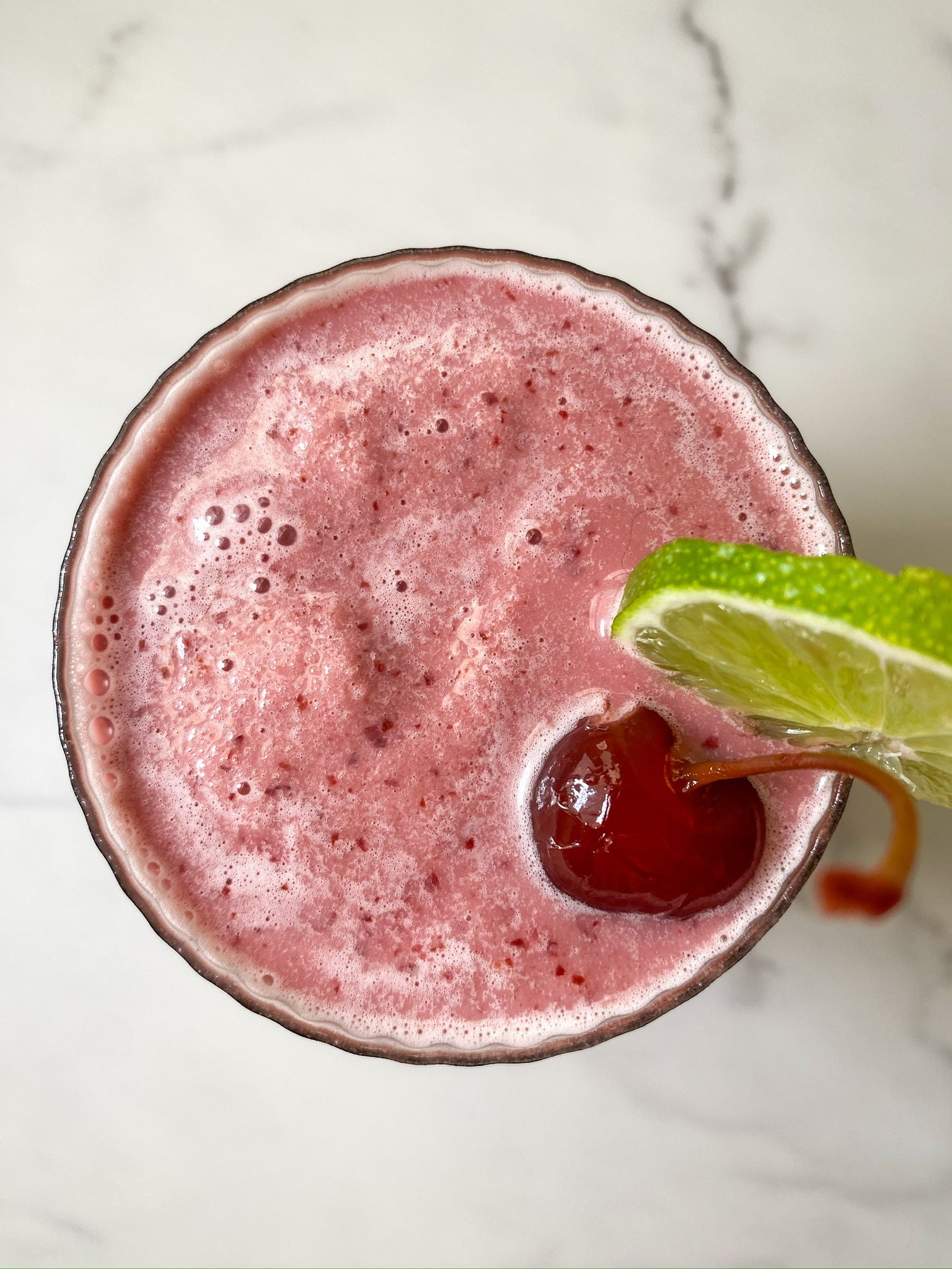 An overhead view of a JOI cherry limeade slushy, garnished with a maraschino cherry and a lime slice.