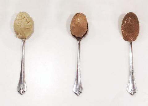 Three spoons hold creamy, light brown JOI nut bases, showcasing different textures and hues.