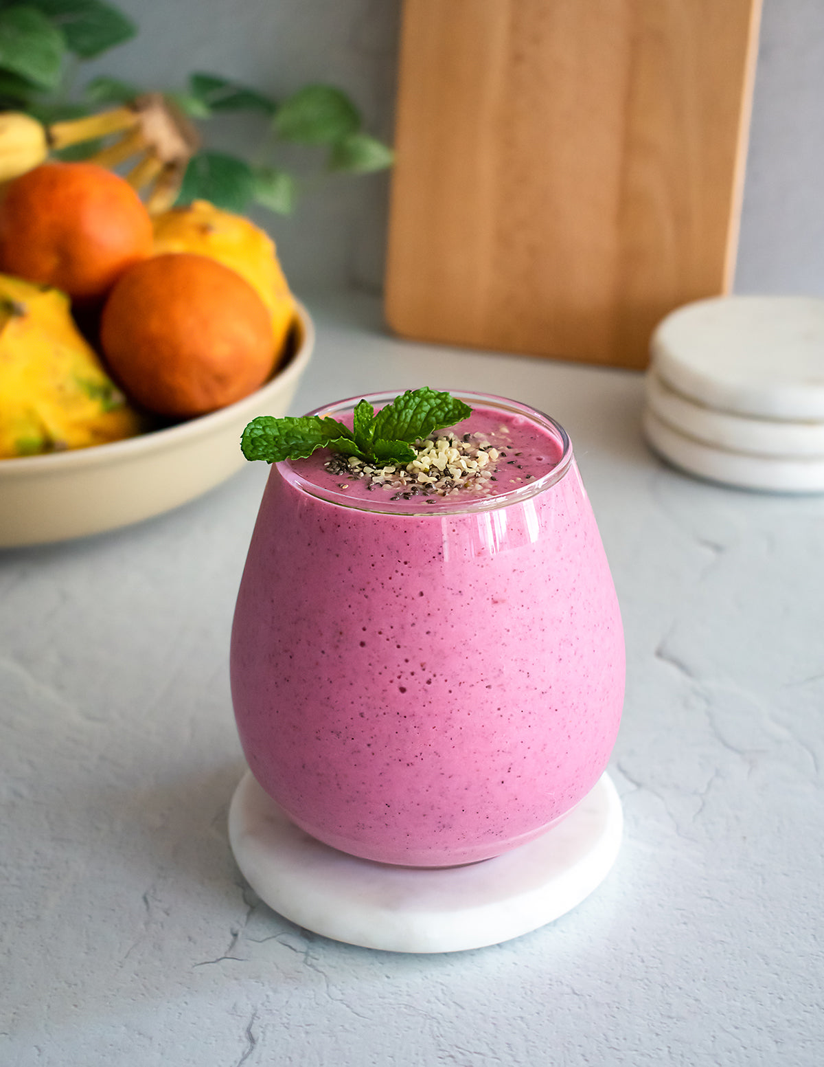 A vibrant pink dragon fruit smoothie, made with JOI plant base, topped with mint and seeds, next to a bowl of fruit.