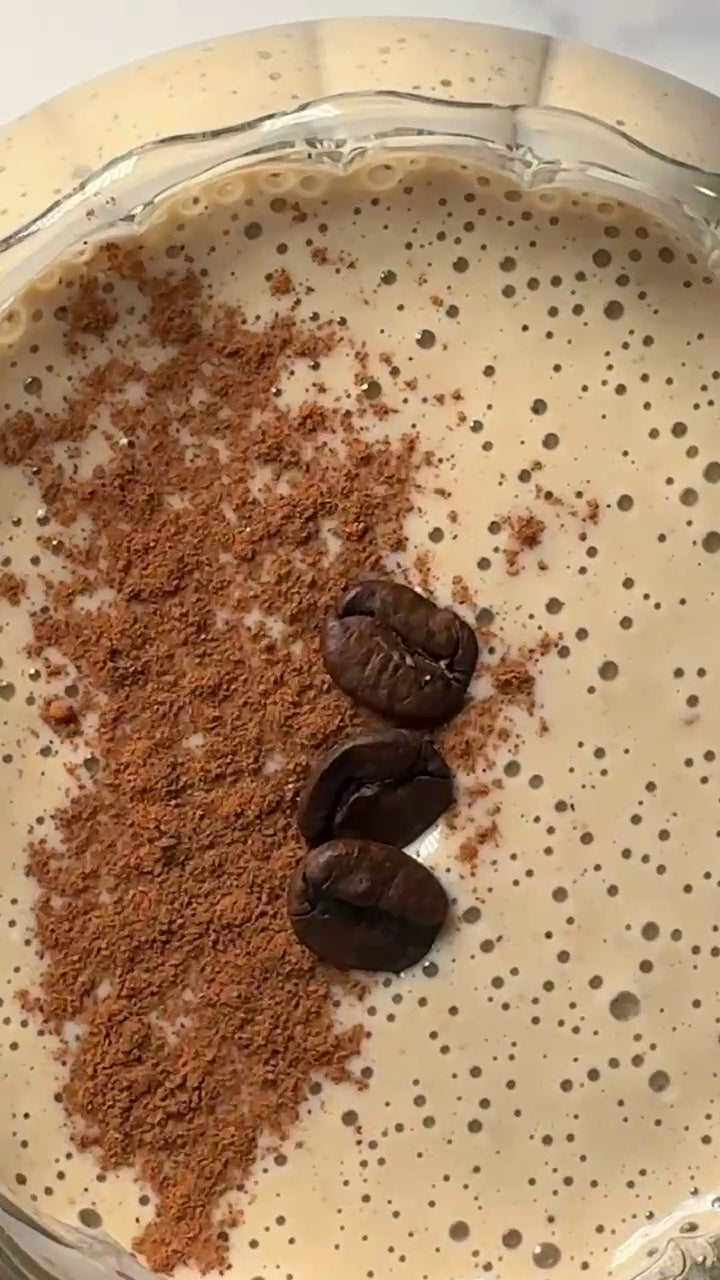 Overhead view of a creamy Tahini Date Coffee Shake, blended with JOI plant base, topped with cocoa powder and coffee beans.