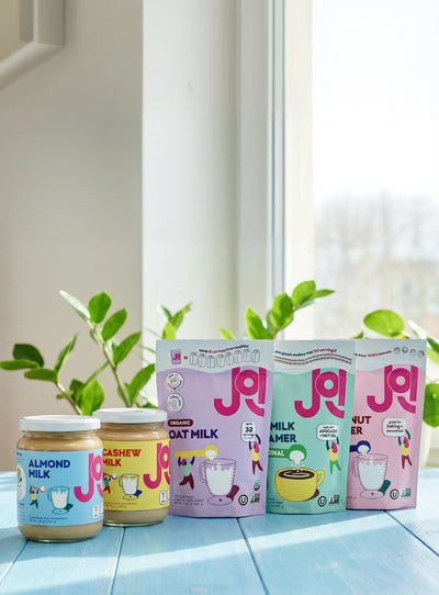 Collection of plant-based milk products including almond, cashew, oat milk, and oat creamer displayed on a table.