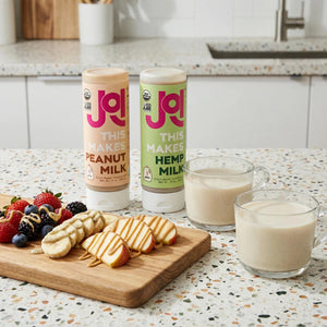 Peanut and hemp milk concentrates displayed with fresh fruit, sliced apples, and creamy plant-based milk.