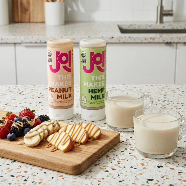 Peanut and hemp milk concentrates displayed with fresh fruit, sliced apples, and creamy plant-based milk.