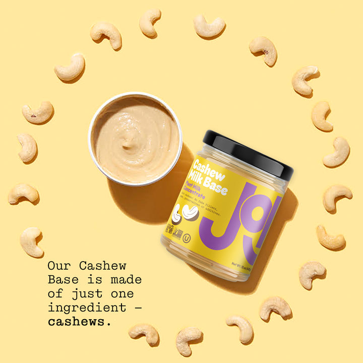 A JOI Cashew Base concentrate tub and a dish of cashew spread, surrounded by loose cashews, on a yellow background, with text, "Our Cashew Base is made of just one ingredient — cashews."