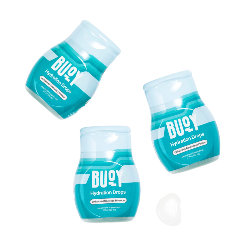 Three BUOY Hydration Drops bottles with a white hydration drop tablet. Labels read “BUOY Hydration Drops” and “Unflavored Beverage Enhancer”.