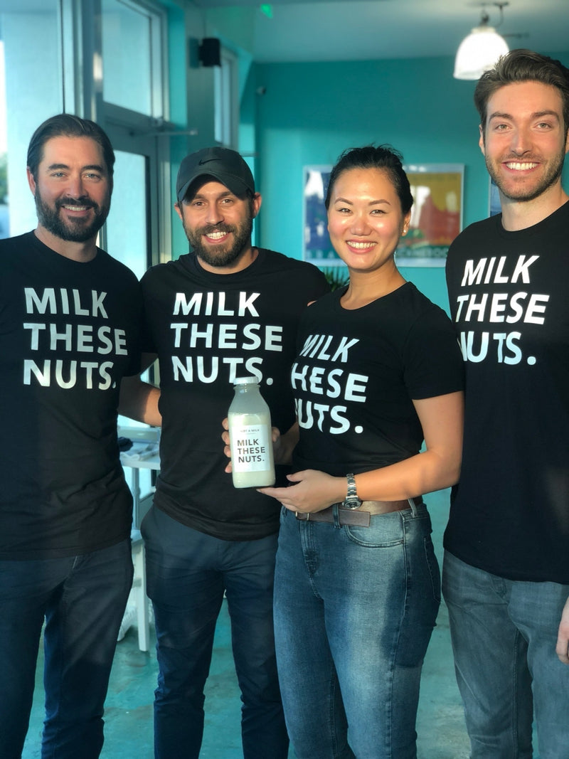 Team members posing together while holding a bottle of Milk These Nuts plant-based milk.