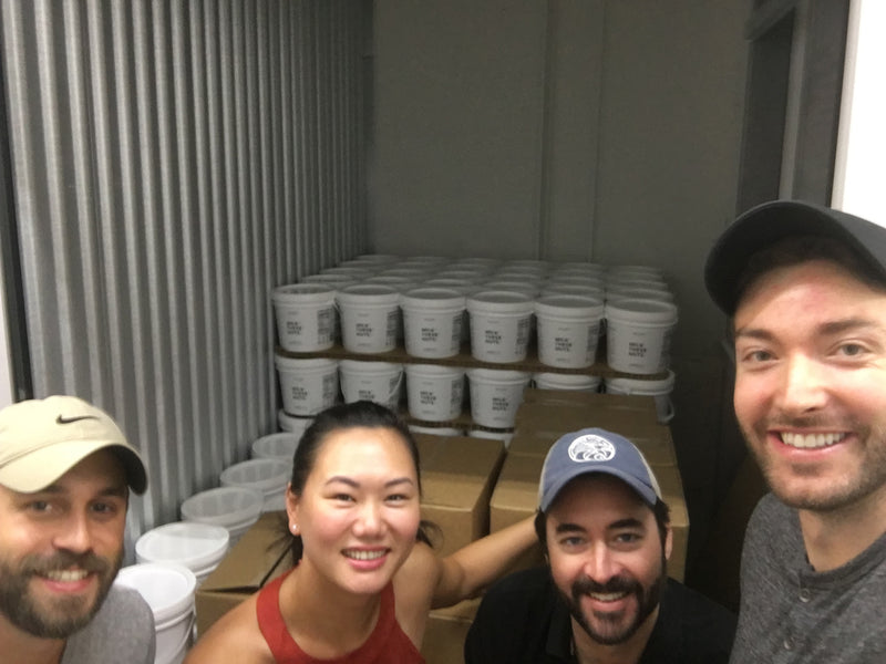 Milk These Nuts team posing in a storage unit stocked with fresh nut milk containers.